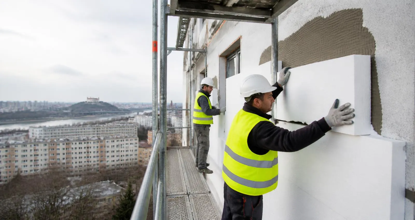 Pracovníci osádzajú izolačné dosky na fasádu bytového domu z lešenia
